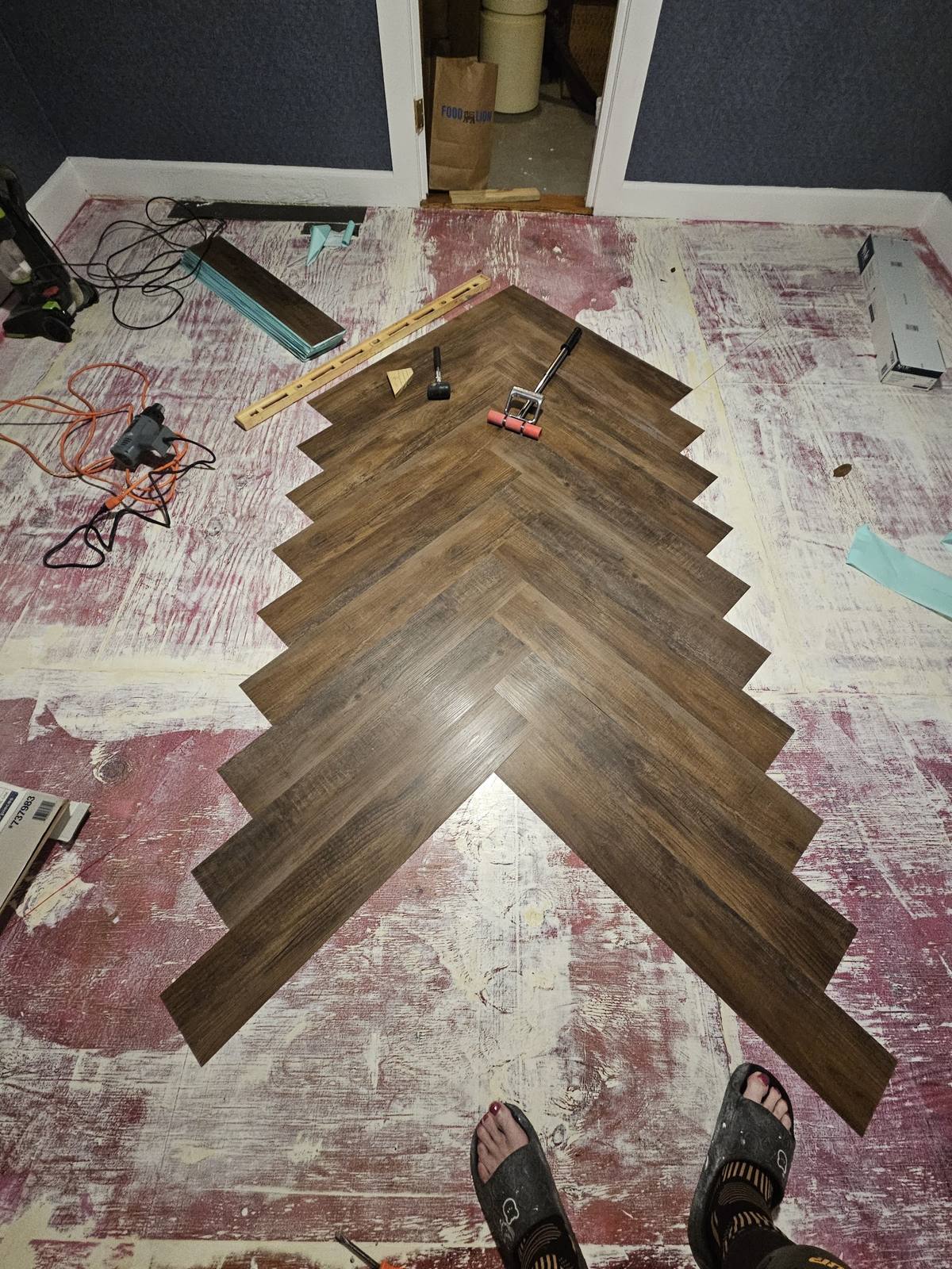 The first dark walnut LVP planks being installed in a herringbone pattern